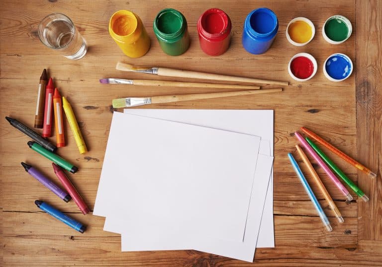 Blank white paper with painting supplies and pencils on a wooden table